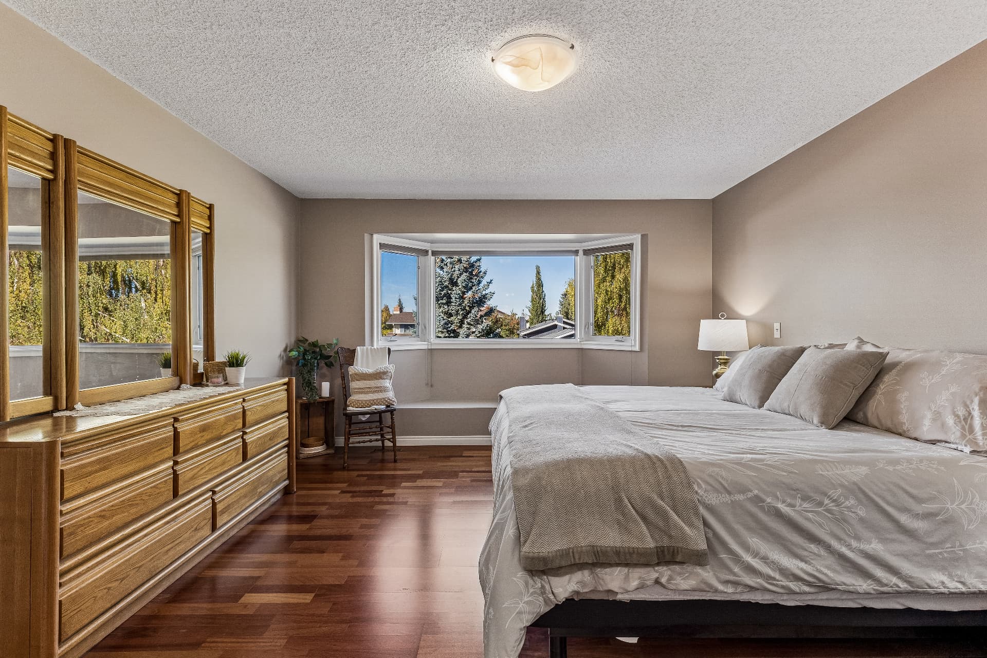 Primary bedroom — hardwood floors and treed views